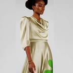 Woman wearing a beige dress with green accents on a plain background