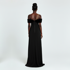 Woman wearing a black off-shoulder gown with a gold chain detail on a white background