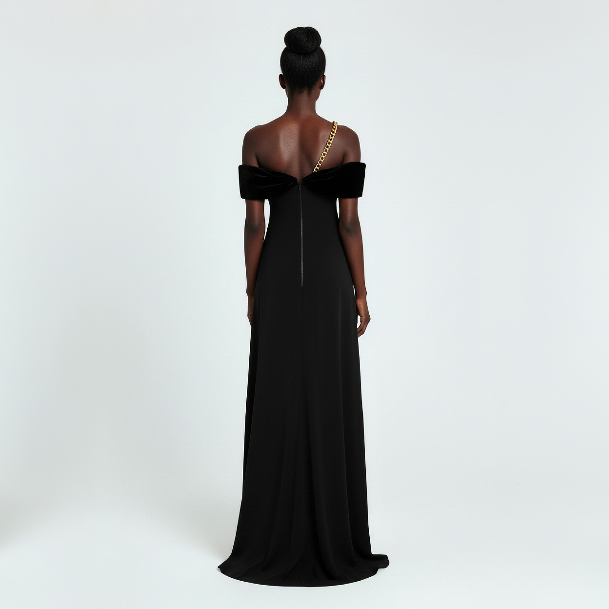 Woman wearing a black off-shoulder gown with a gold chain detail on a white background