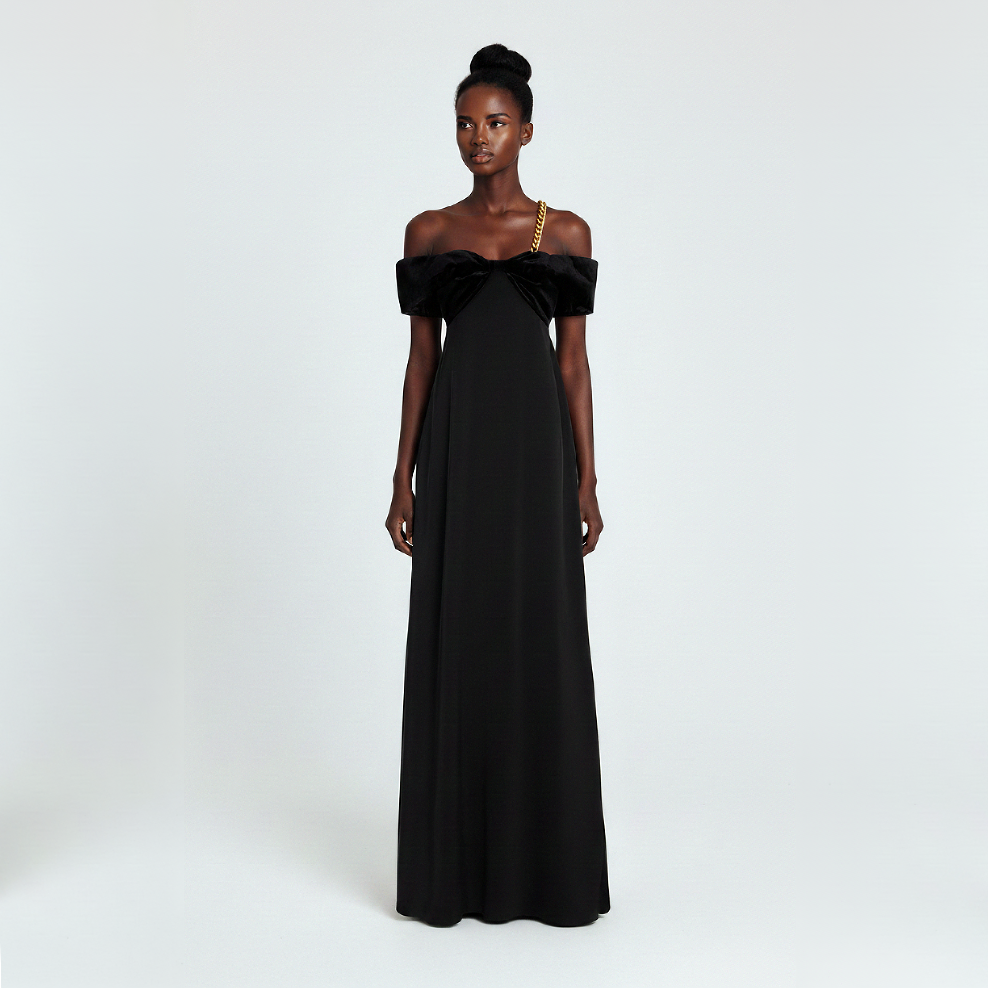 Woman wearing a black off-shoulder gown with a gold chain on a white background