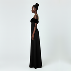 Woman wearing a black off-shoulder gown with gold accents on a white background