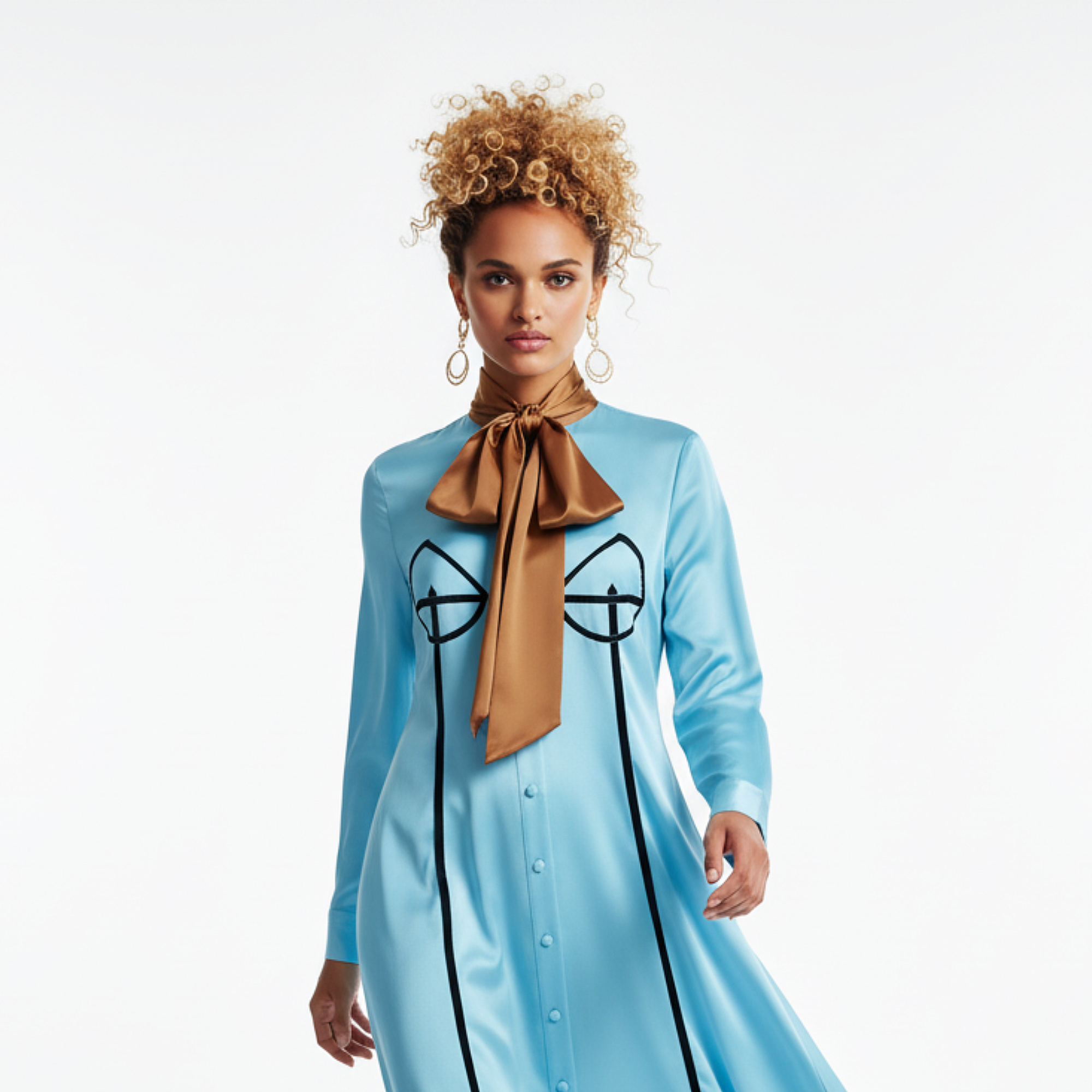 Woman wearing a light blue dress with black designs and a brown scarf, standing against a white background.