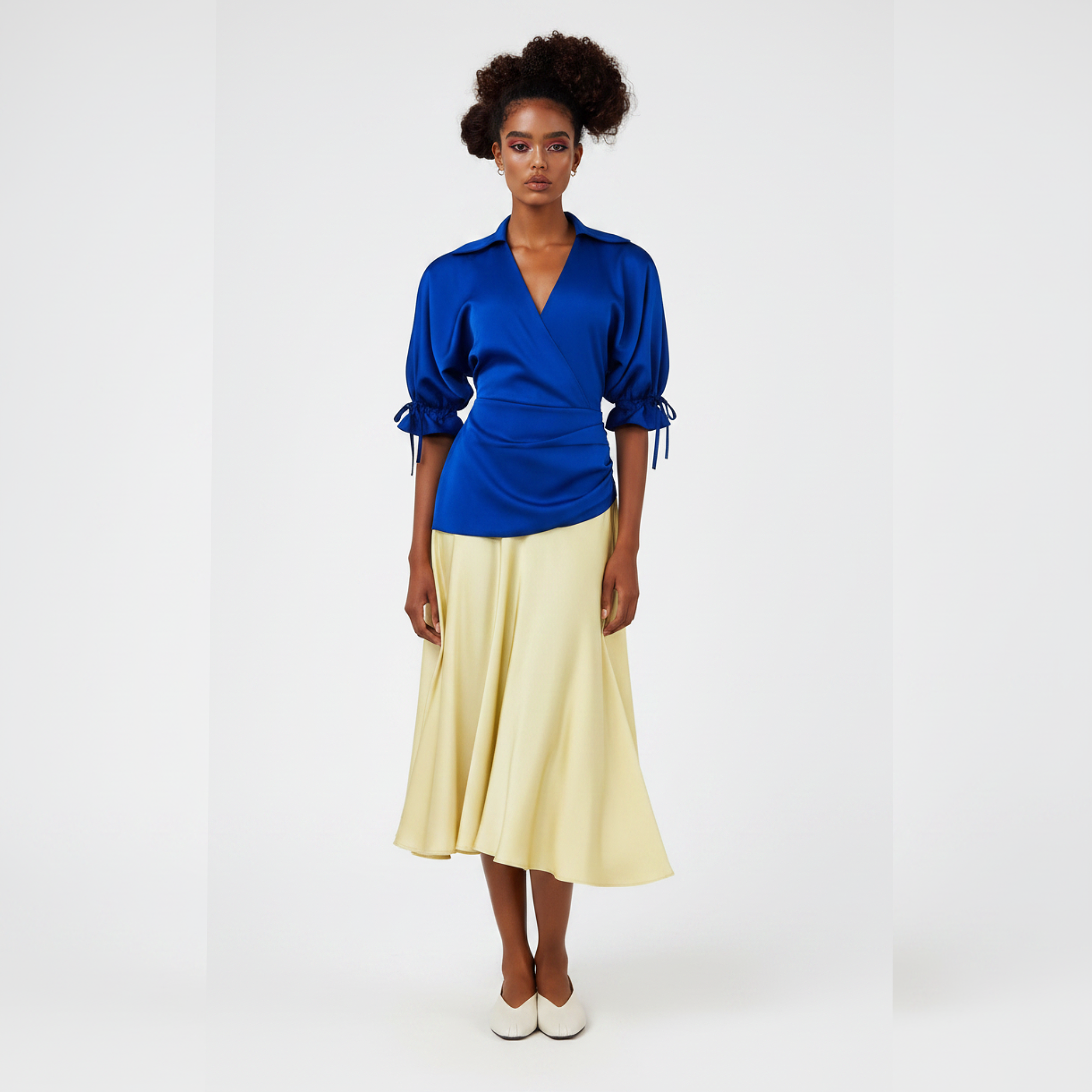 Woman wearing a dress with a blue top and yellow skirt holding a beige handbag on a white background