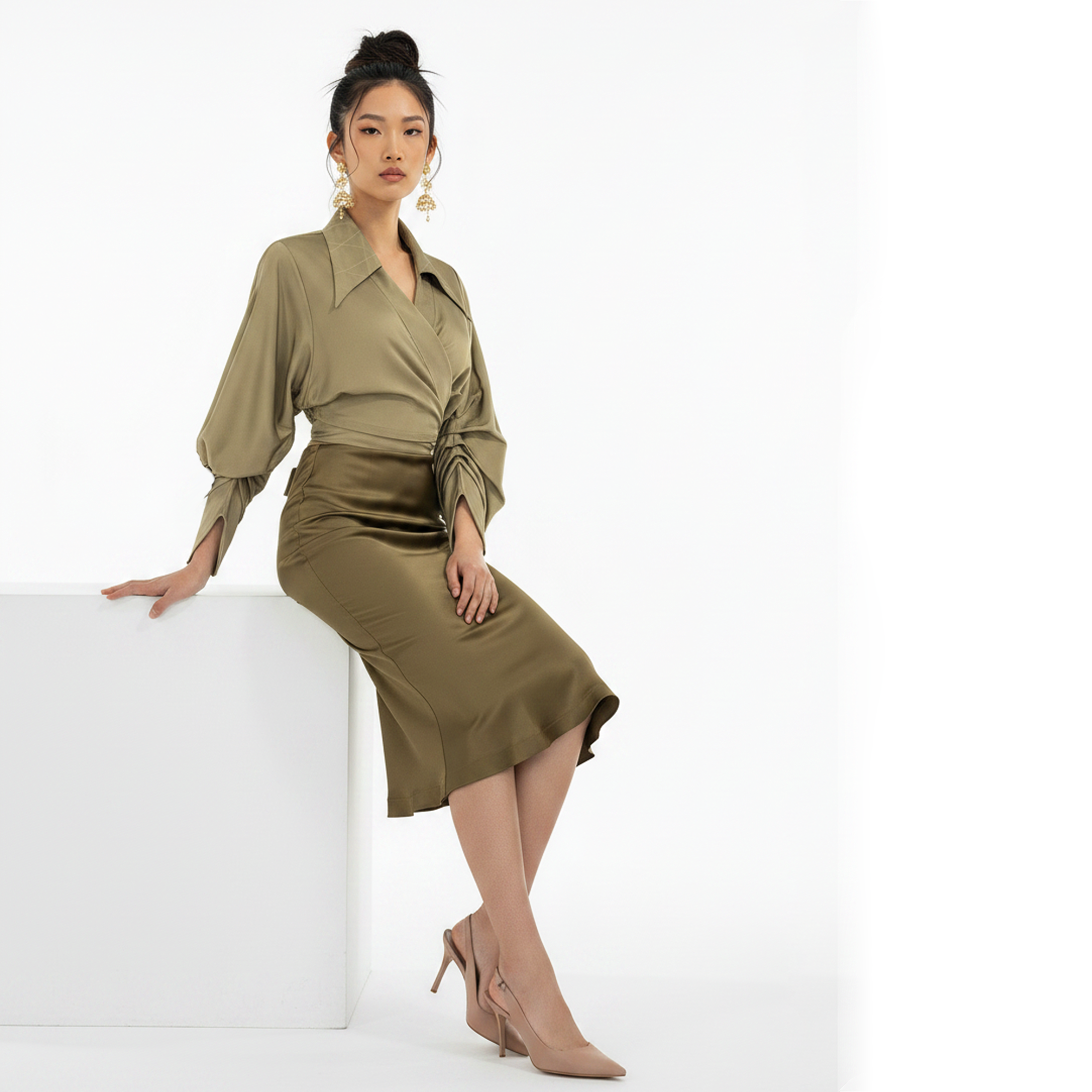Woman wearing a green outfit sitting on a white block against a white background