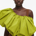 Woman wearing a bright green off-shoulder top with a plain background