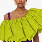 Woman wearing a bright green off-shoulder top with purple accents on a white background