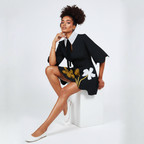 Woman in a black outfit with floral patterns sitting on a white cube against a white background