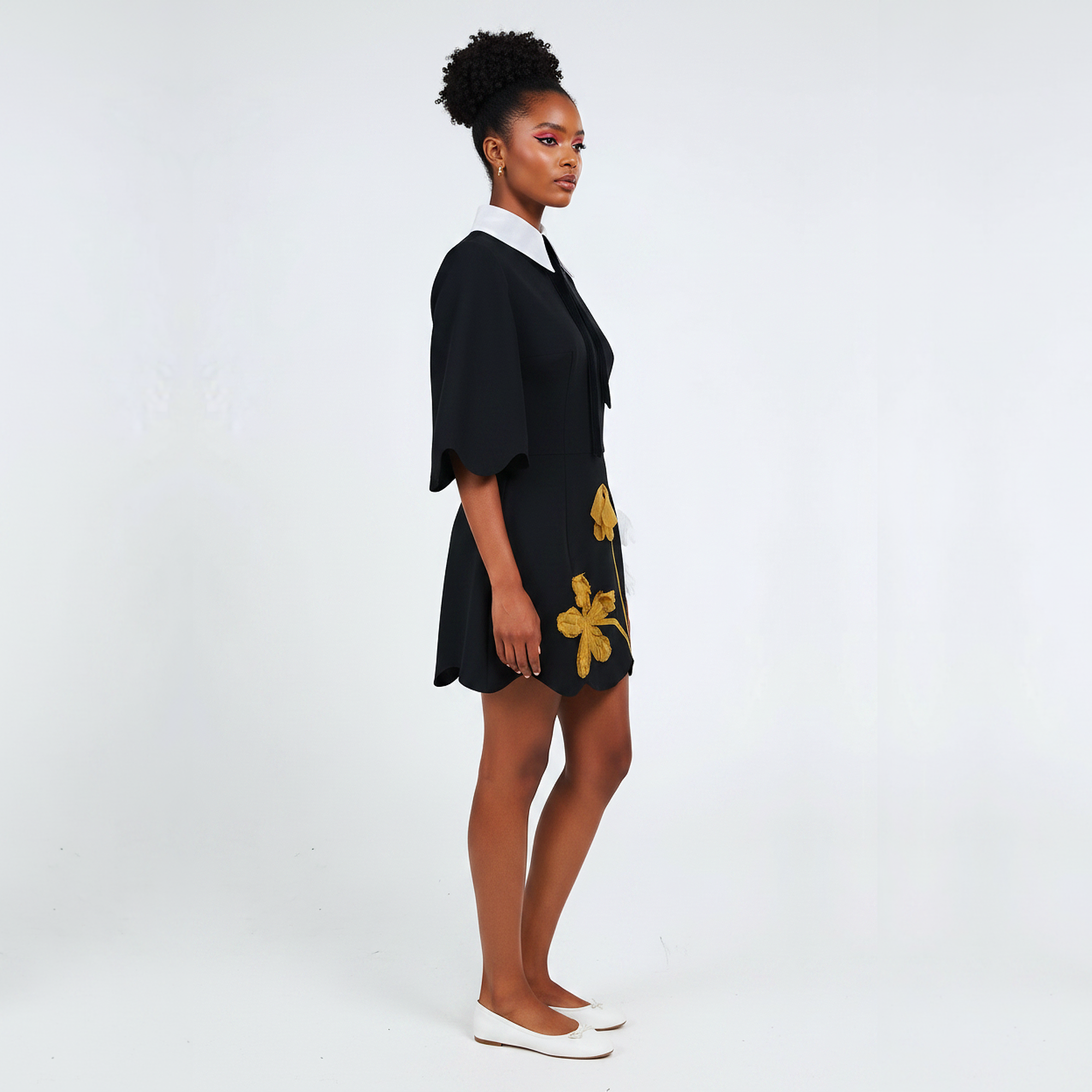 Woman wearing a black dress with yellow floral patterns on a white background